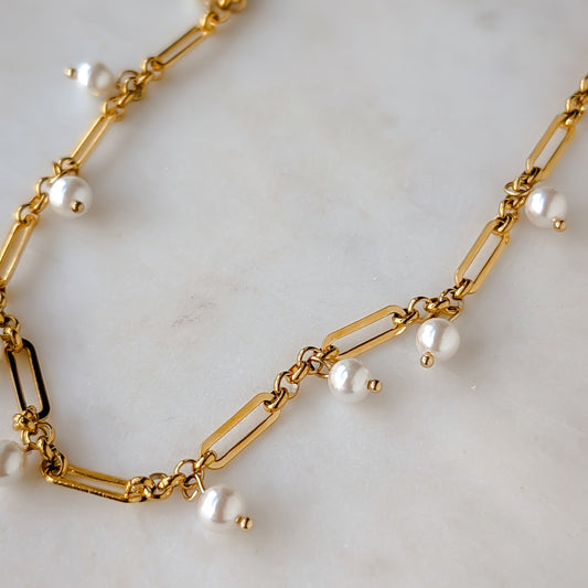 Gold chain necklace with pearls on a light marble background