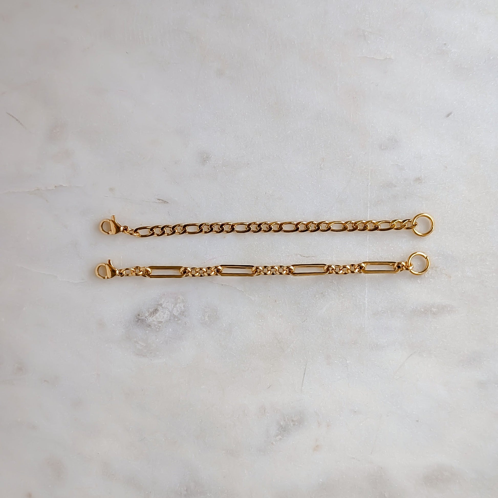 Two gold extension chain bracelets on a light marble surface