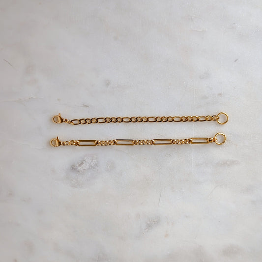 Two gold extension chain bracelets on a light marble surface