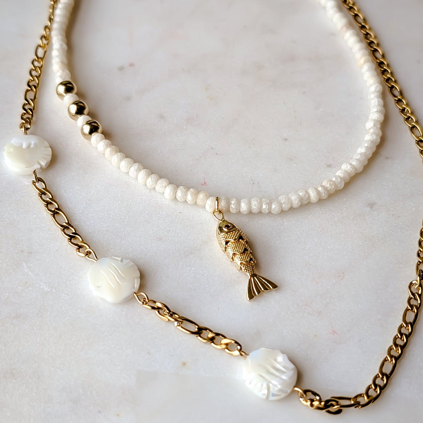 Two necklaces with pearls and gold chains on a marble surface