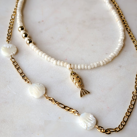 Two necklaces with pearls and gold chains on a marble surface