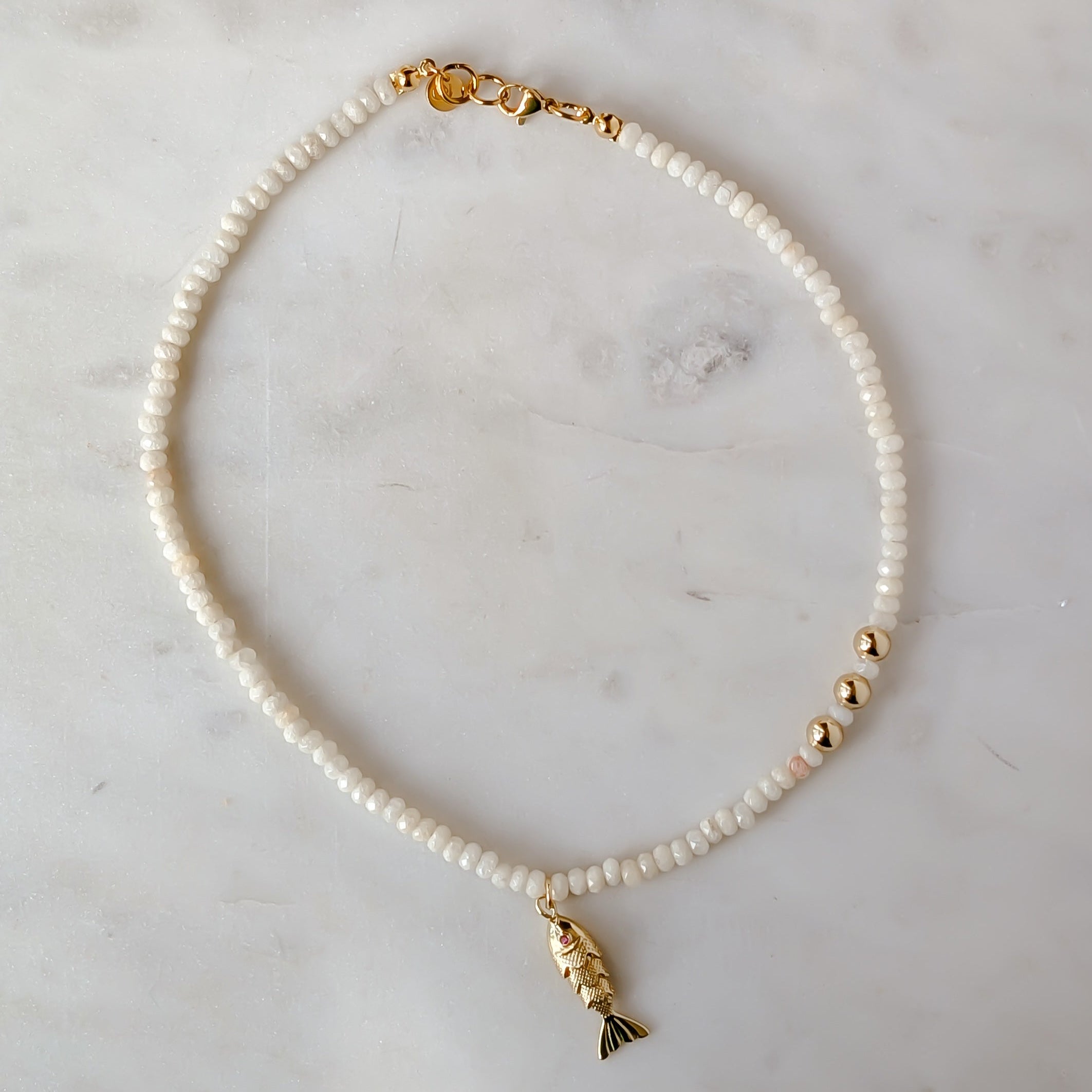 Everyday beaded necklace with a gold fish charm on a marble surface