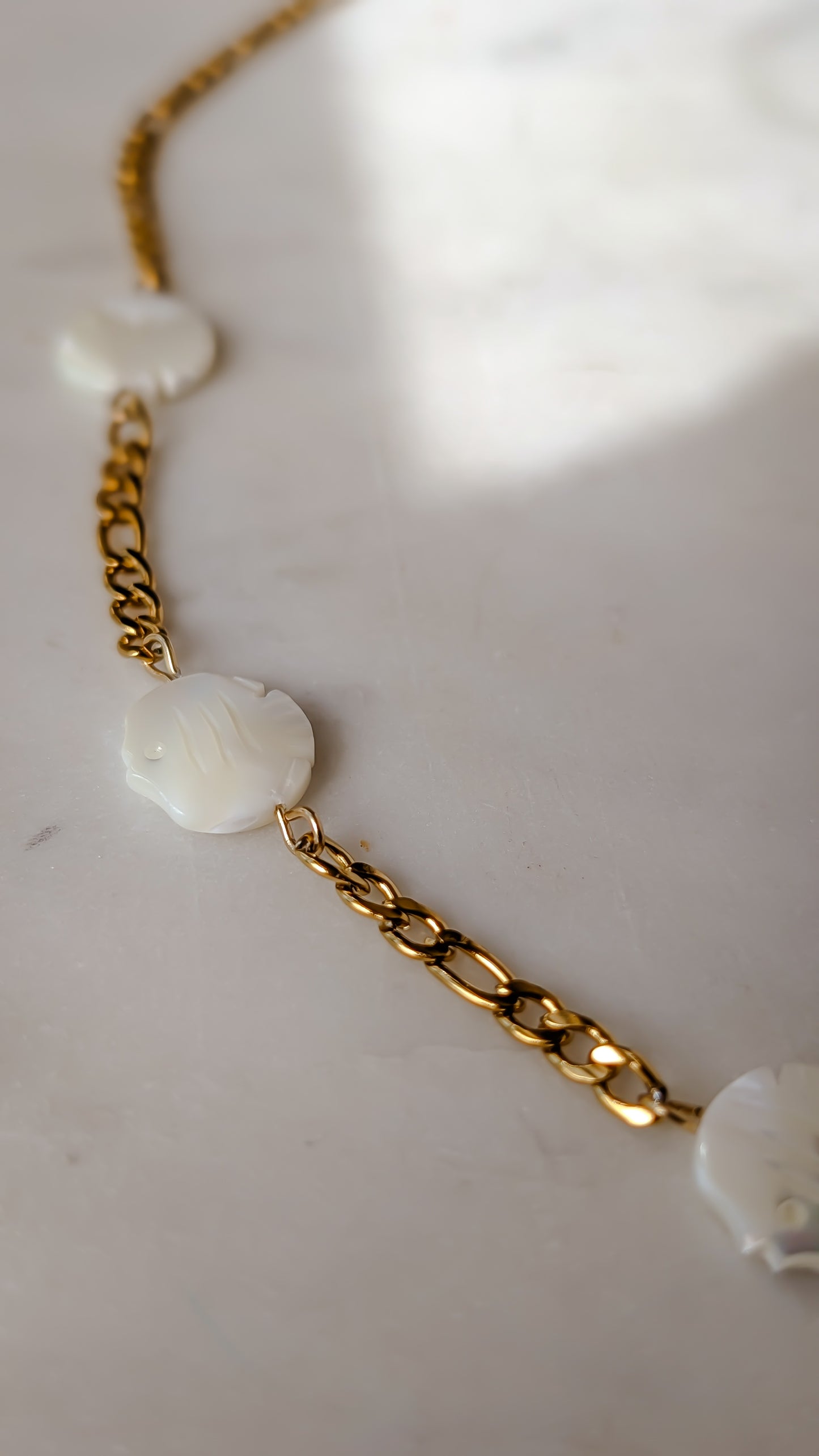 Gold chain necklace with white floral pendants on a light background