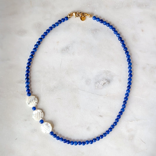 Blue beaded necklace with white accents on a marble surface