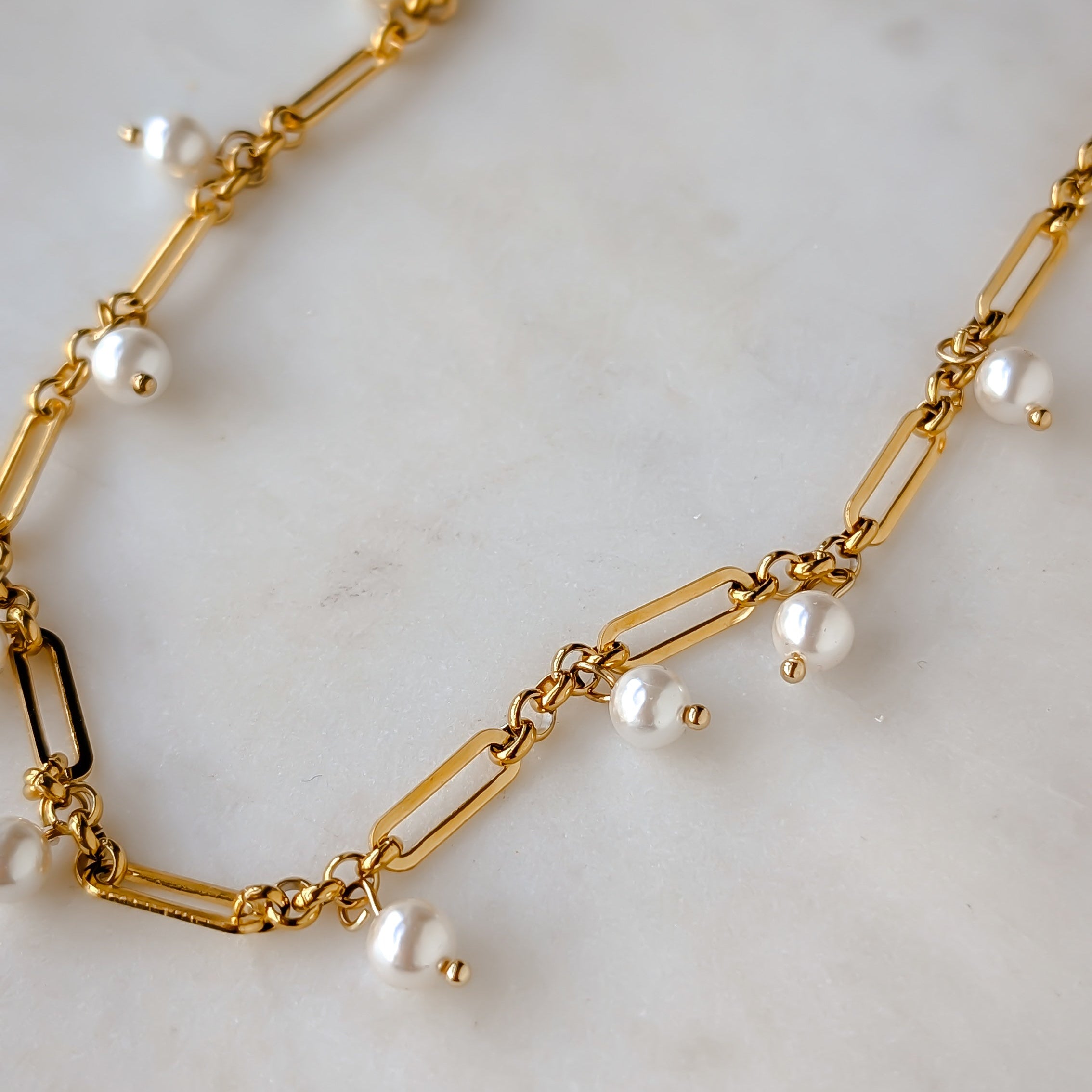 Gold chain necklace with pearls on a light marble background