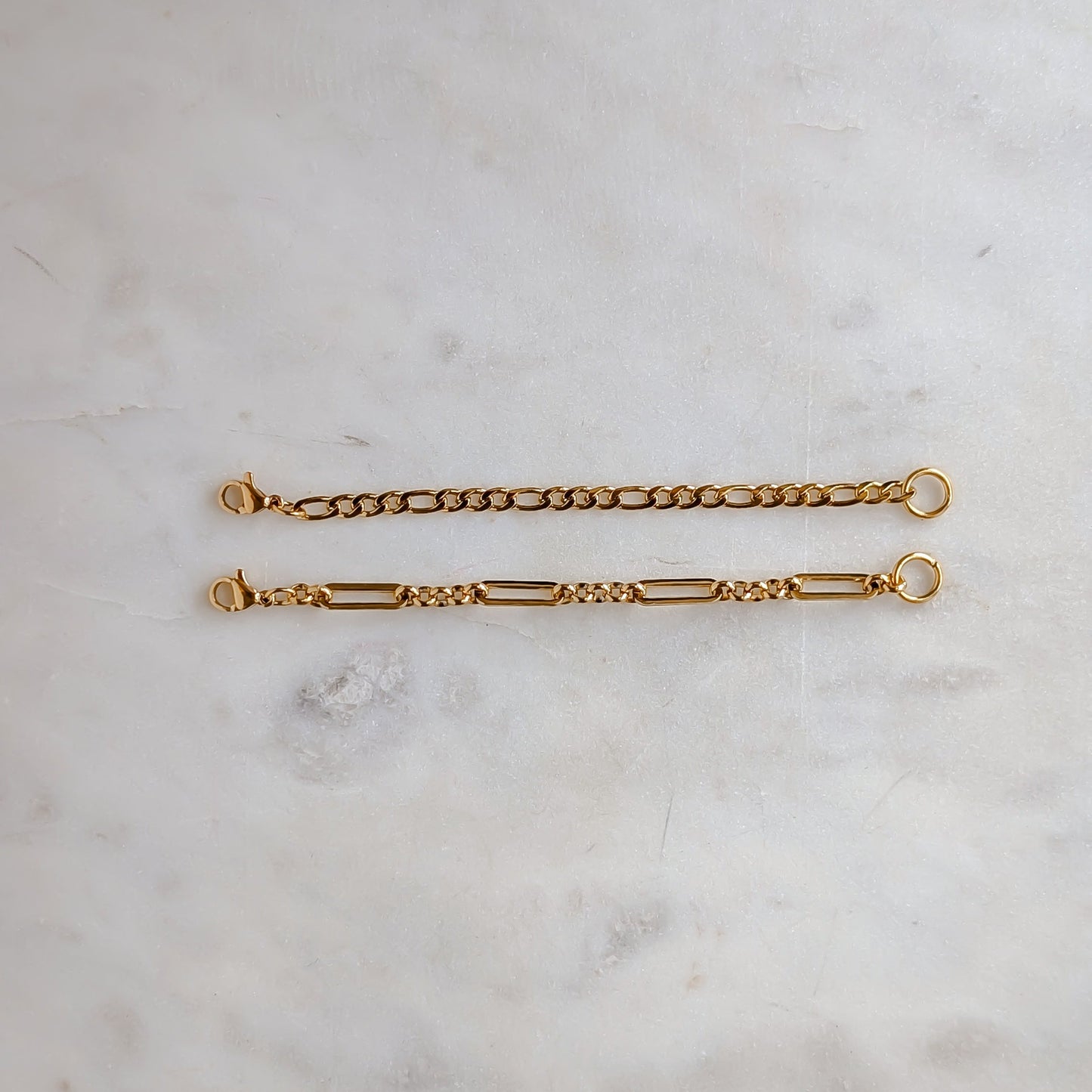 Two gold extension chain bracelets on a light marble surface