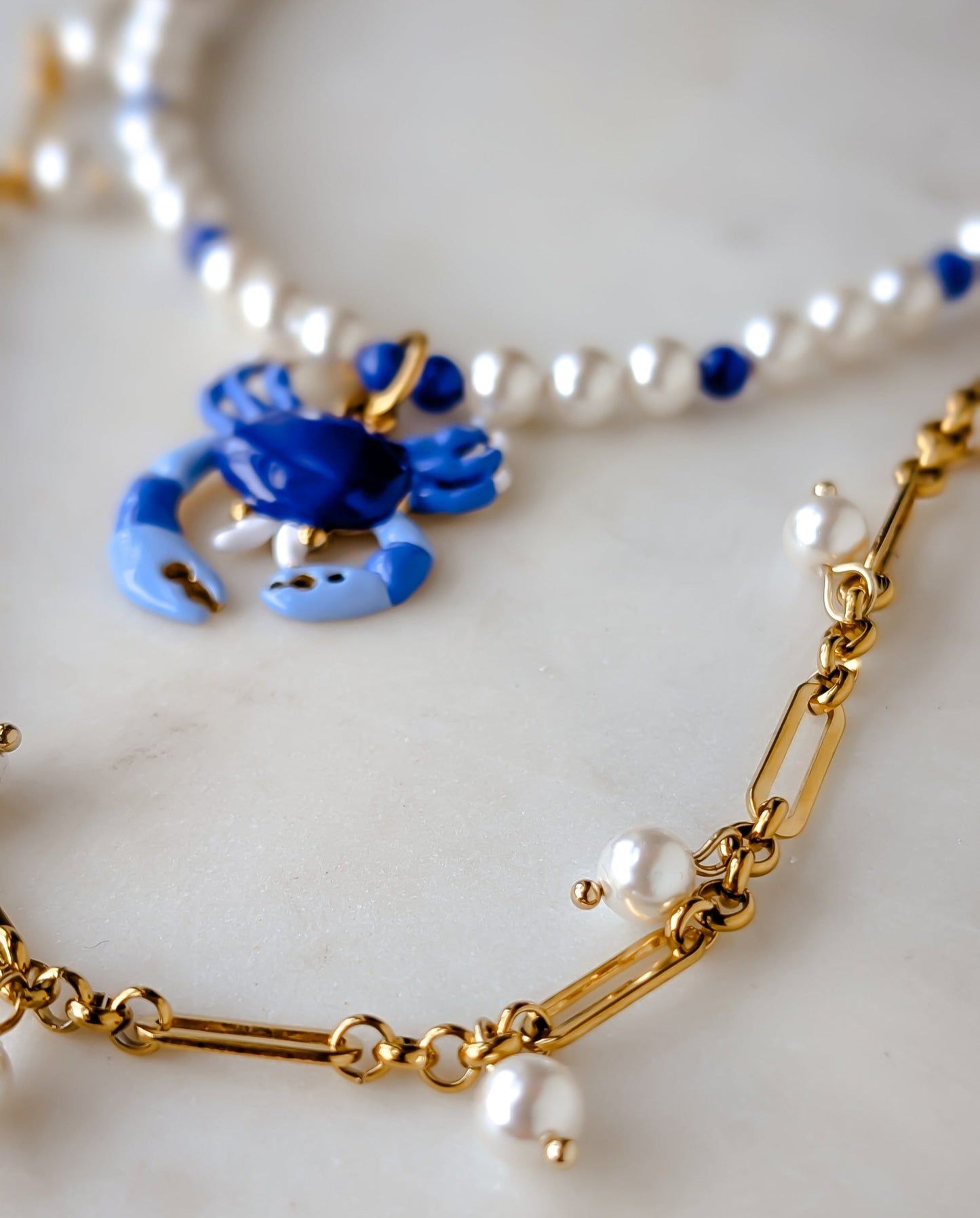 Gold chain necklace with blue crab pendant and pearl necklace on a white background