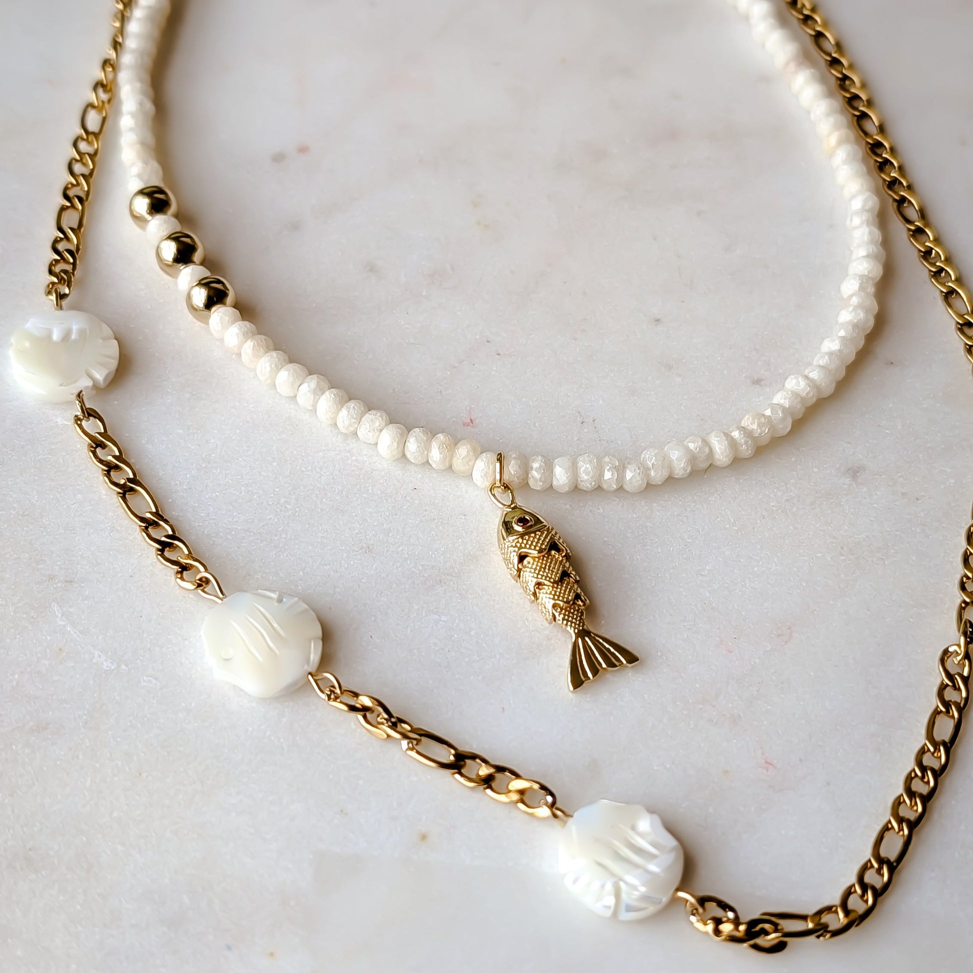 Two necklaces with pearls and gold chains on a marble surface
