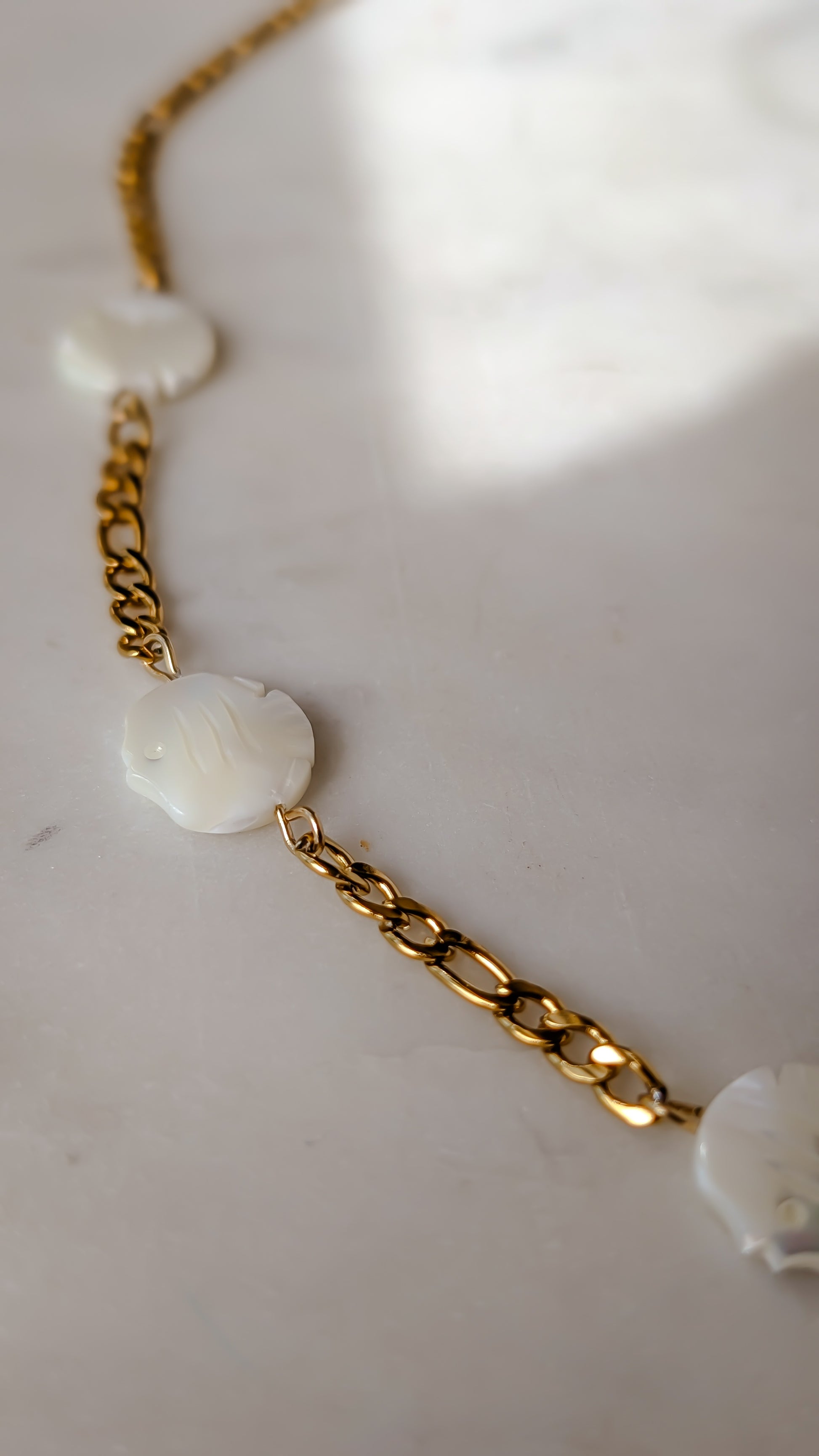 Gold chain necklace with white floral pendants on a light background