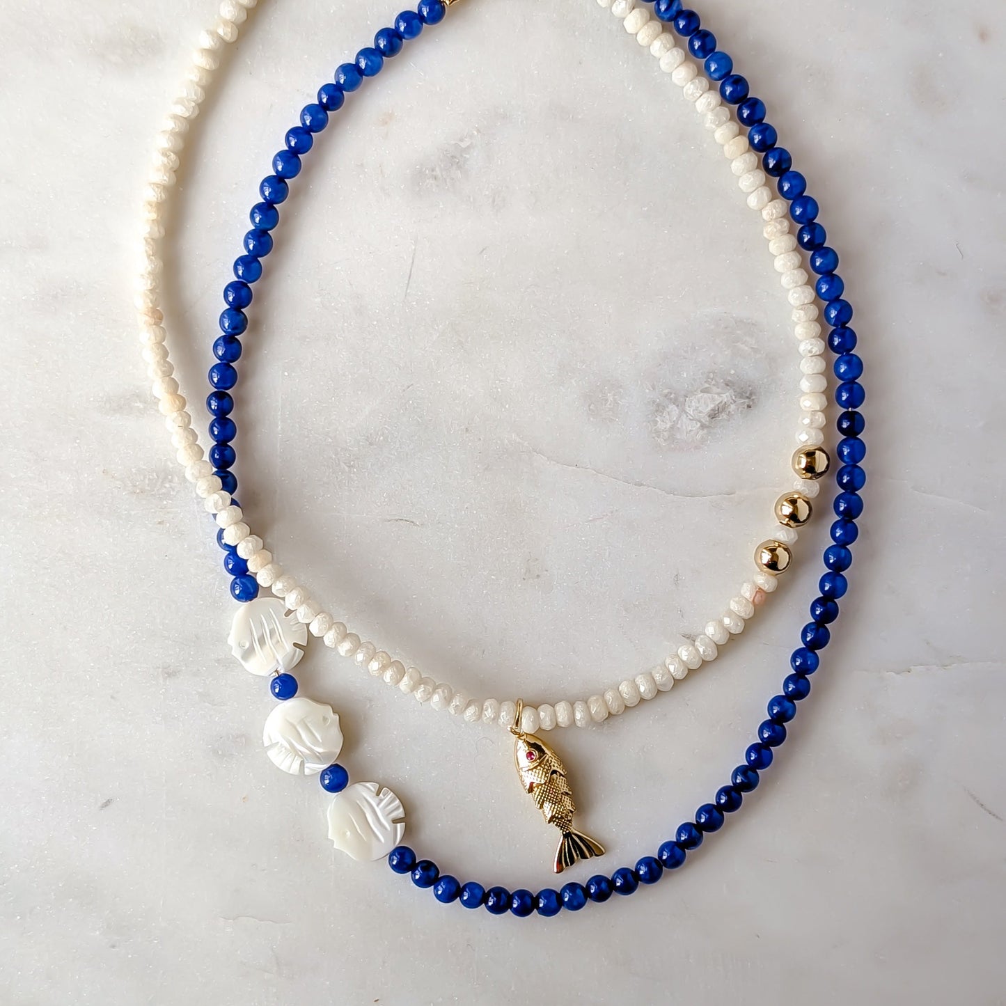 Two necklaces, one blue and one pearl, on a marble surface