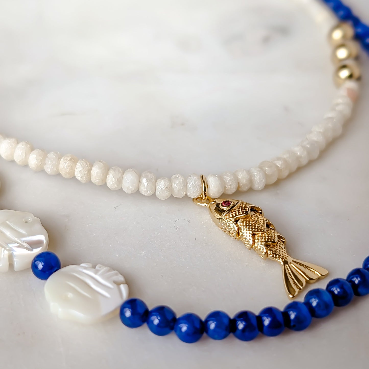 Two beaded necklaces with blue and gold elements on a marble surface