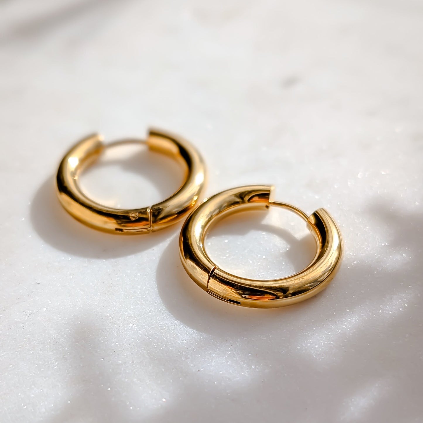 Gold hoop earrings on a white marble background