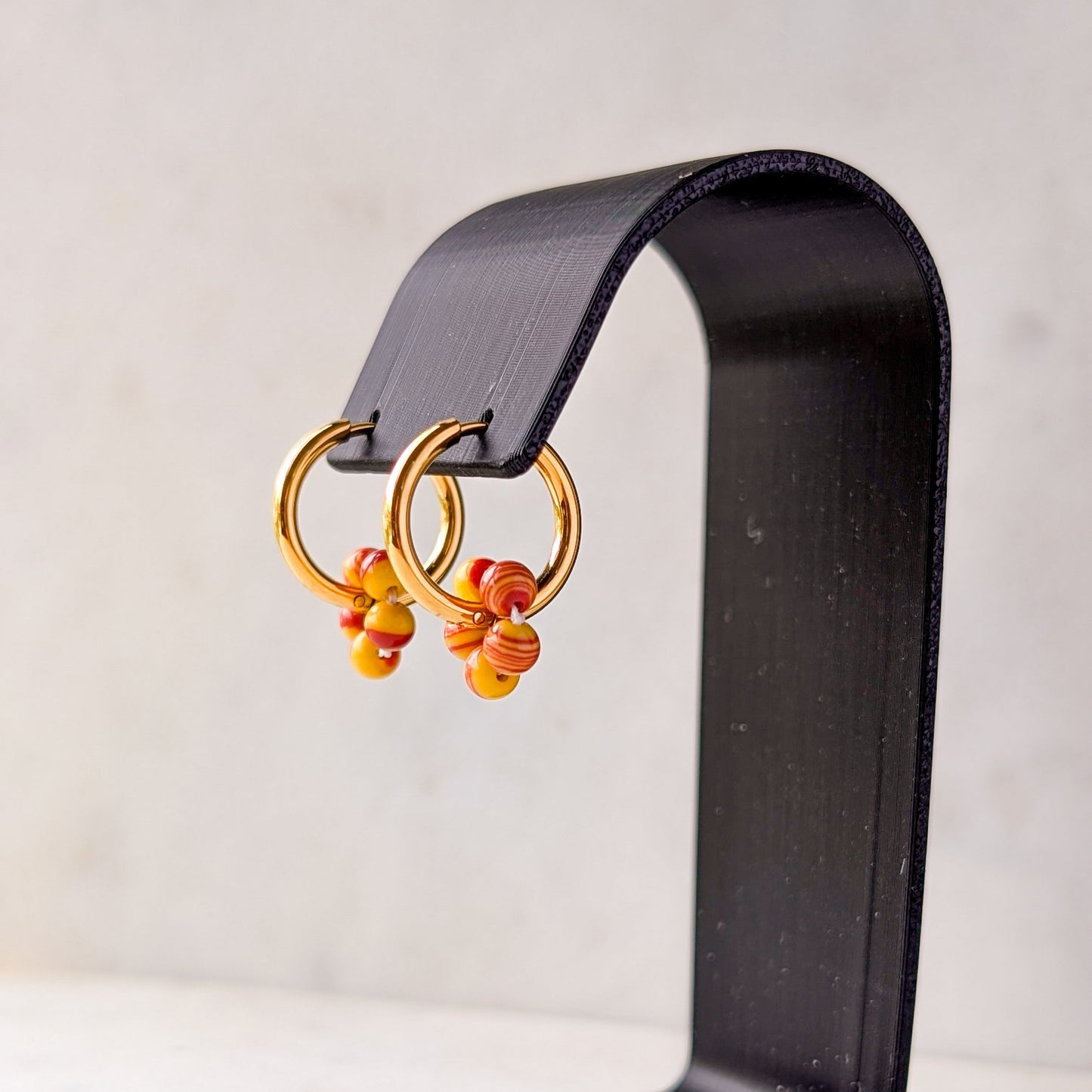 Pair of gold hoop earrings with orange flowers on a black stand against a white background