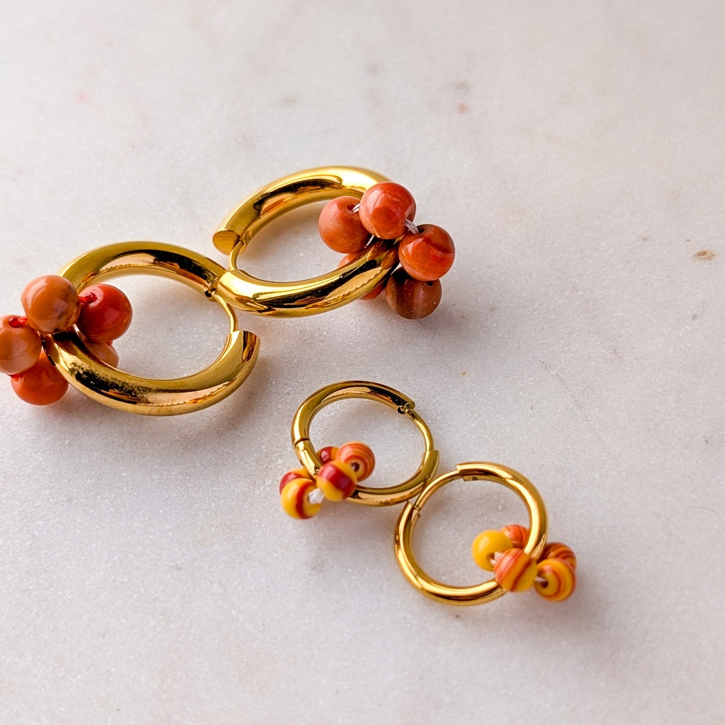 Gold hoop earrings with coral beads on a light marble background