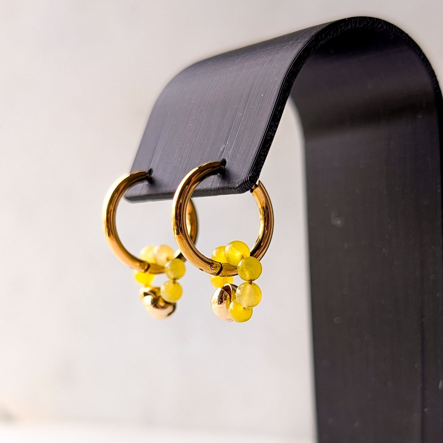 Gold hoop earrings with yellow accents on a black stand against a white background